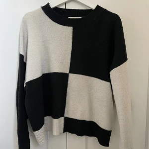 Svart och vit rutig stickad tröja - Säljer en stickad tröja med stora svarta och vita rutor. Tröjan har rund halsringning, lång ärm och en loose passform. Inte alls stikig i matrialet