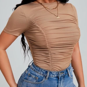 Beige ribbad croppad topp - Säljer en beige ribbad topp med snygg rynkad effekt framtill och på sidorna. Modellen är croppad med korta ärmar och rund halsringning. Materialet är mjukt och stretchigt, perfekt att styla med jeans eller kjol för en trendig look.