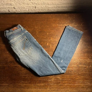 Dondup jeans George - W30 L32 Snygga blå jeans från Dondup, tillverkade i Italien. Klassisk femficksmodell med kontrastsömmar och diskret logodetalj vid bakfickan. Jeansen har en rak passform och är gjorda i mjukt denimtyg som sitter skönt hela dagen.