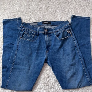 Blå Replay jeans straight fit - Säljer ett par klassiska blå jeans från Replay med raka ben och normal passform. Jeansen har fem fickor, snygga kontrastsömmar och Replay-logga på myntfickan. Tillverkade i mjukt denimtyg som sitter skönt med bra passform. Har en lagning på knäet som en skräddare sytt, väldigt snyggt lagad. Se bild på lagningen på sista bilen!