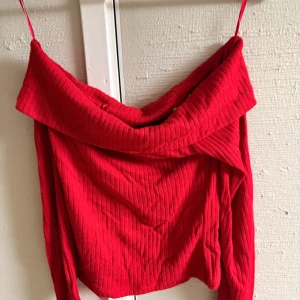 Röd ribbad offshoulder topp Cache Cache - Snygg röd ribbad topp från Cache Cache med offshoulder-design och långa ärmar. Materialet är mjukt och stretchigt, perfekt för att skapa en cool och trendig look. Den breda kragen ger extra attityd och toppen har en figurnära passform.