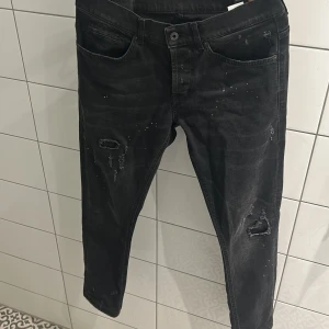 Dondup George  - Svarta jeans med skinny fit och coola slitningar samt små vita färgstänk. Klassisk femficksmodell med dragkedja och knapp. Jeansen har en smal passform och är tillverkade i stretchigt jeansmaterial för en bekväm känsla. storlek 33, bara att höra av sig vid frågor och funderingar 