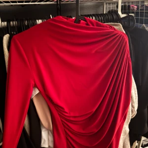 Röd draperad långärmad klänning Mistix - Säljer en snygg röd långärmad klänning från Mistix med cool drapering på ena sidan. Klänningen har en figurnära passform och är tillverkad i ett mjukt, stretchigt material som känns bekvämt. Perfekt för dig som vill sticka ut med en statement-look.
