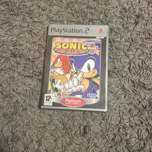 Sonic Mega Collection Plus (PlayStation 2) - Sonic Mega Collection Plus till PlayStation 2 i Platinum-version. Komplett med fodral, manual och skiva. Skivan ser ut att vara i gott skick, inga synliga repor. Perfekt för retrospelare och samlare av klassiska Sonic-spel.