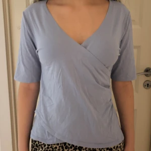 Ljuslila omlottopp från Bondelid - Supersöt ljuslila omlottopp från Bondelid i mjuk bomull. Toppen har v-ringning, korta ärmar och en snygg omlottdesign framtill som ger en schysst passform