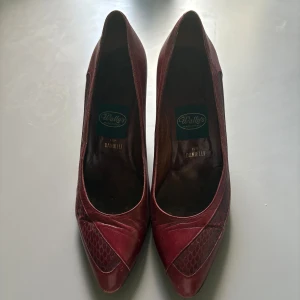 Vinröda pumps från Wally's Made in Italy - Snygga vinröda pumps från Wally's per Danielli, tillverkade i Italien. Skorna har spetsig tå, låg klack och är gjorda i äkta skinn med detaljer i ormskinnsmönster framtill. Perfekta för dig som vill ha en klassisk och elegant look.