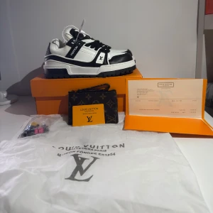 Louis Vuitton svartvita sneakers - Exklusiva Louis Vuitton sneakers i svart och vitt med tydliga LV-loggor och detaljer. Skorna har en chunky sula, snörning och är tillverkade i en mix av skinn och textil. Snygg kontrast mellan svart och vitt, samt klassiska Louis Vuitton-detaljer på sidan och sulan.