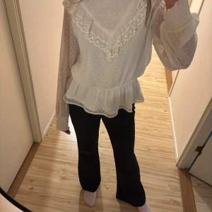 Vit blus med spets och volang - Säljer en söt vit blus med prickigt mönster, volangdetaljer och spets längs bröstet. Blusen har långärmade, lätt transparenta ärmar med smock vid handlederna och en liten volangkant i halsen med svart kant. Storlek 158, men passar mig som vanligtvis har storlek xs-s.