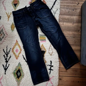 Mörkblå jeans från Firetrap - Snygga mörkblå jeans från Firetrap med kontrastsömmar och klassisk femficksdesign. Jeansen har raka ben och detaljer som knappstängning och logoknappar. Perfekta för dig som gillar en stilren och enkel look.