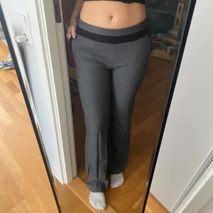Grå kostymbyxor från H&M, strl 36 - Snygga grå kostymbyxor från H&M i storlek 36. Byxorna har svarta detaljer i midjan och vid fickorna, samt en rak och något utsvängd passform. Perfekta för en clean och stilren look. Materialet är mjukt och följsamt.