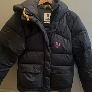 Grå/grön dunjacka Fjällräven Expedition - Säljer en mörkgrå/grön Fjällräven Expedition Down  dunjacka. Färgen ser svart ut på bilderna, men syns bäst på bild 3. Beroende på lite ljus upplevs den antingen grå eller grön. Färgen heter ”basalt”. Använd under två vintrar, och köpt för 7000. Jackan är superfin! 