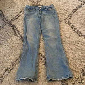 Ljusblå bootcut jeans - Säljer ett par ljusblå jeans med klassisk bootcut-modell. Jeansen har fem fickor, knapp och dragkedja framtill samt lätt slitna benslut för en avslappnad look. Perfekta för dig som gillar retrovibbar och bekväm passform.