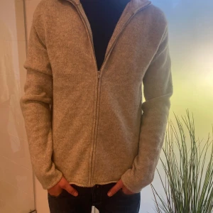 Grå kofta från Polo Ralph Lauren - Snygg beige kofta från Polo Ralph Lauren i 100% lammull. Modellen har dragkedja framtill och långärmad passform. Perfekt för lager-på-lager och chillare dagar. Enkel och stilren design som funkar till det mesta.