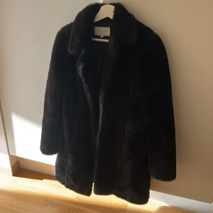 Svart pälsjacka från VILA, stl 36 - Mysig svart pälsjacka från VILA i storlek 36. Jackan har klassisk krage, helsvart foder och en fluffig, lyxig känsla. Perfekt för kalla dagar när du vill ha en stilren och trendig look. Långärmad och rak modell som ger en snygg siluett.