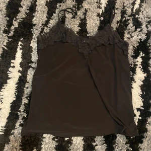 Svart linnetopp med spets från Amisu - Säljer en svart linnetopp från Amisu i storlek XS. Toppen har tunna axelband och vacker spetsdetalj längs urringningen. Materialet är mjukt och lätt, perfekt för en stilren look. Enkel att matcha med både jeans och kjol.