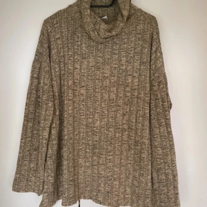 Beige ribbad polotröja - Mysig beige polotröja med ribbad struktur och lös passform. Tröjan har lång ärm och hög krage som ger en chill och avslappnad vibe. Perfekt för lager-på-lager under kyliga dagar.