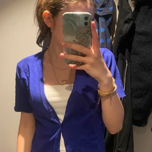 Kornblå kofta med kort ärm - Snygg kornblå kofta med korta ärmar och djup v-ringning. Koftan har knappar framtill och är i ett tunt, mjukt material som känns skönt mot huden. Perfekt att slänga över ett linne eller t-shirt för en chill look.