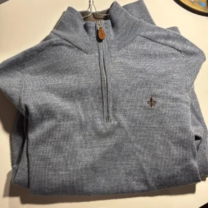 Blå tröja Morris - Snygg blå stickad tröja från Morris. Tröjan har half zip med läderdetalj vid dragkedjan och en broderad logga på bröstet. Perfekt för lager-på-lager och passar till både jeans och chinos. Aldrig använd. Pris kan diskuteras vid snabb affär.