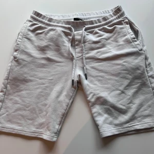 Vita shorts från Prada med snörning - Snygga vita shorts från Prada i mjuk bomull. De har en relaxed passform, elastisk midja med snörning och praktiska fickor. På baksidan finns en diskret Prada-logga med röd detalj. Perfekta för chill dagar och sommarhäng.