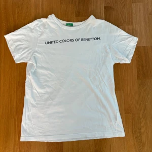 Vit t-shirt från United Colors of Benetton - Vit t-shirt från United Colors of Benetton med svart tryck på bröstet. Hittar ingen storlek i tröjan men passar mig bra som har storlek xs-S i kläder. Tröjan är skrynklig men stryker såklart den innan jag postar. 