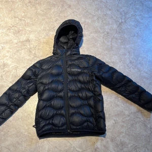 Svart dunjacka Peak Performance 170 - Svart dunjacka från Peak Performance i storlek 170. Jackan har huva, dragkedja framtill och ett quiltat mönster som ger en cool look. Jackan är sparsamt använd. Priset är ej hugget i sten😃 Kom med prisförslag och frågor!🙏