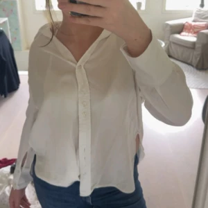 Vit skjorta från Zara  - Säljer en vit skjorta från Zara i mjukt, glansigt material med  krage och knappar framtill. Skjortan har lång ärm, slits i sidorna och en lite loose fit.