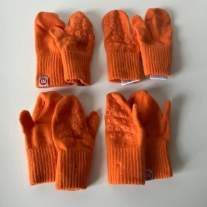 Orange tumvantar från PAX  - Fyra par orange tumvantar från PAX med ribbad mudd. Vantarna är tillverkade av akryl, ull, polyester och elastan, vilket gör dem både mjuka och stretchiga. 