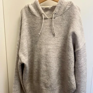 Ljusgrå stickad hoodie från Gina Tricot - Mysig ljusgrå stickad hoodie från Gina Tricot med huva och snörning. Tröjan har lång ärm och ribbade muddar. Perfekt för dig som gillar en chill och enkel stil. Passar till allt och är superbekväm att dra på sig när det är kallt ute. Kan se lite ”hängig” ut på bilden men de är pga att den är så mjuk men sitter bra på! 146/152 men sitter som xs!