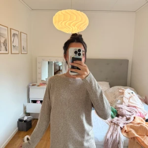 Beige stickad tröja med rund hals - Mysig beige stickad tröja med rundad hals och långa ärmar. Tröjan har ribbade muddar vid ärmslut och nederkant, vilket ger en chill och enkel look. Perfekt att slänga på sig när det är lite kyligt ute.