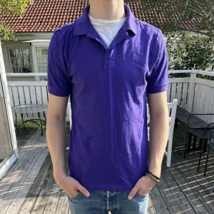 Piké - Snygg lila piké t-shirt med klassisk krage och korta ärmar. T-shirten är enkel och stilren utan tryck eller mönster, perfekt för en avslappnad look. Tillverkad i mjuk bomull som känns skön mot huden.