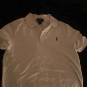 Vit pikétröja från Polo Ralph Lauren - Vit pikétröja från Polo Ralph Lauren med klassisk krage och korta ärmar. Tröjan har den ikoniska broderade loggan på bröstet och är gjord i mjuk bomull. Perfekt för en clean och stilren look. vet ej om äkta elr nt