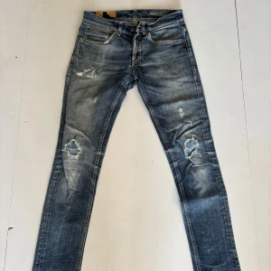 Blå skinny jeans från Dondup, stl 31 - Säljer ett par blå skinny jeans från George i storlek 31. Jeansen har slitna detaljer och hål på knäna för en cool, avslappnad look. Klassisk femficksmodell med dragkedja och knapp. Perfekta för dig som gillar en smal passform och streetstil. Lagade på knän men ser bra ut