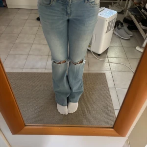 Bootcut jeans med slitna knän från Nelly - Ljusblå bootcut jeans från Nelly med låg midja och snygga slitningar vid knäna. Jeansen har fickor med lock bak och klassisk femficksdesign. Tillverkade i jeansmaterial och perfekta för en avslappnad look. Knappt använda säljer pga att dom blivit förstora för mig och inte passar längre.