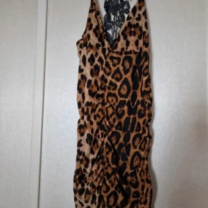 Leopardmönstrad långt linne/kort klänning med spets - Snyggt längre linne/ kortare klänning med leopardmönster och djup v-ringning. Klänningen har smala axelband och en svart spetsdetalj på ryggen som ger en extra touch. Perfekt för dig som vill sticka ut med ett djuriskt mönster och cool design. Aldrig an änd, har lappar kvar.