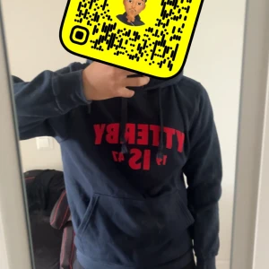 Mörkblå Ytterby hoodie med röd text - Mörkblå hoodie från Ytterby med stor röd text framtill och årtalet 1947. Klassisk känguruficka, snörning i huvan och mjukt material. Perfekt för chill dagar eller när du vill ha en enkel men snygg look.