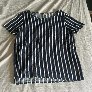 Randig t-shirt från Jacqueline de Yong - Snygg t-shirt med marinblå och vita vertikala ränder från Jacqueline de Yong. Modellen har rund hals och korta ärmar, perfekt för en chill och stilren look. Materialet är mjukt och känns lätt mot huden, passar dig som gillar enkel men trendig design.