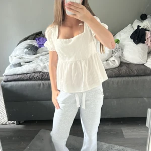 Vit blus med puffärm och knyt i ryggen - Supersöt vit blus med fyrkantig ringning, puffärmar och volang nedtill. Blusen har knytband i ryggen och är tillverkad i ett lätt, strukturerat tyg som känns luftigt. Finns tyvärr ingen lapp vart den är ifrån men det är en S eller Xs 💗