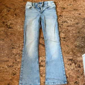 Ljusblå bootcut jeans från H&M - Snygga ljusblå bootcut jeans från H&M med låg midja och justerbar midja. Klassisk femficksmodell med coola bakfickor med lock och knapp. Jeansen är i stretchig denim och har slitningar framtill för en trendig look.