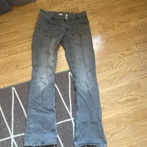 Grå jeansbyxor från Gina Tricot - Snygga grå jeansbyxor från Gina Tricot med utsvängda ben och två små fickor framtill. Byxorna har dubbla knappar i midjan och klassiska bakfickor. Perfekta för dig som gillar en enkel men cool stil.