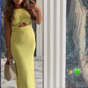 Gul långklänning med twist-detalj - Säljer en snygg gul långklänning med twistad detalj framtill och cut-out under bysten. Klänningen har en figurnära passform och är tillverkad i ett strukturerat tyg. Perfekt för dig som vill sticka ut med en trendig look och coola detaljer.