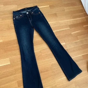 True Religion bootcut jeans mörkblå - Mörkblå jeans från True Religion med klassiska kontrastsömmar och snygga fickdetaljer bak. Modellen har bootcut-ben och låg midja, tillverkade i stretchig denim för skön passform. Ikoniska loggan på bakfickan och patch på linningen.