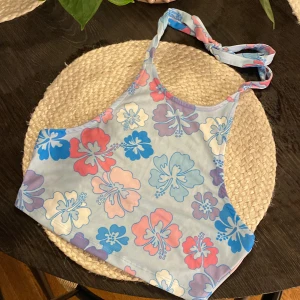 Blommig topp från NA-KD - Supersöt topp med öppen rygg från NA-KD i storlek XS med blommigt mönster i blått, lila, rosa och vitt. Modellen har hög halsringning och knyt i nacken.