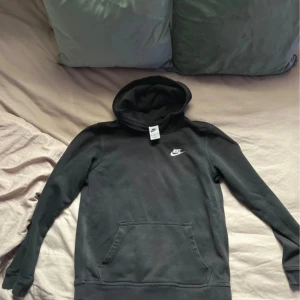 Svart hoodie från Nike XL - Svart hoodie från Nike i storlek XL men passar dig som är Xs- S, med klassisk vit Nike-logga broderad på bröstet. Tröjan har huva, magficka och långa ärmar. Materialet är mjuk bomull och polyester, perfekt för chill dagar eller när du vill ha en enkel streetstyle-look.