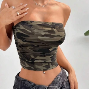 Camouflage bandeau tubtopp - Säljer en snygg bandeau tubtopp med camouflage-mönster i gröna och svarta toner. Toppen är axelbandslös och tight, perfekt för dig som vill ha en cool och trendig look. Materialet är mjukt och stretchigt för en bekväm passform. Aldrig använd!!!