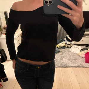 Svart offshoulder långärmad topp - Säljer en svart långärmad topp med offshoulder-design och smal passform. Toppen har en enkel, stilren look med rak nederkant och är tillverkad i ett mjukt material som sitter skönt mot kroppen. Perfekt för dig som gillar minimalistisk stil och vill ha något som sticker ut med sin asymmetriska axel.