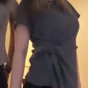 Mörkgrå blus med knyt i midjan - Snygg mörkgrå blus med korta ärmar och ett brett knytband i midjan som ger en cool siluett. Blusen har en enkel, stilren design och är perfekt för dig som gillar att sticka ut med detaljer. Materialet känns mjukt och följsamt mot kroppen.