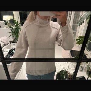 Beige polotröja i ull/kashmir från H&M - Säljer en beige polotröja från H&M i mjuk ull- och kashmirblandning. Tröjan har ribbade muddar vid ärmslut och nederkant samt en hög polokrage. Perfekt för dig som gillar stilrena och mysiga plagg med lite lyxig känsla.