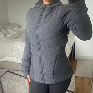 Grå quiltad pufferjacka med huva - Snygg grå Gymshark pufferjacka med quiltade paneler och ribbade sidor. Jackan har huva med snörning, hel dragkedja framtill och långa ärmar med muddar. Perfekt för kyliga dagar och har en clean, sportig look som funkar till många stilar 🖤
