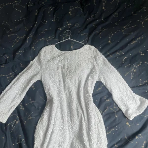 Vit glittrig klänning med svart rosett - Den virala superfina vita klänningen med glittriga paljetter över hela tyget och lång ärm. Baktill sitter en stor svart rosett som ger en extra snygg detalj. Säljer då den är något för kort på mig som är 172cm. 