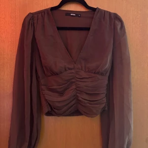 Brun omlott blus från Bik Bok XS - Säljer en brun blus från Bik Bok i storlek XS. Blusen har omlott-design med djup v-ringning, långa puffärmar och snygg rynkning framtill som ger en cool croppad look. Materialet är lätt och luftigt, perfekt för att styla med höga jeans eller kjol.